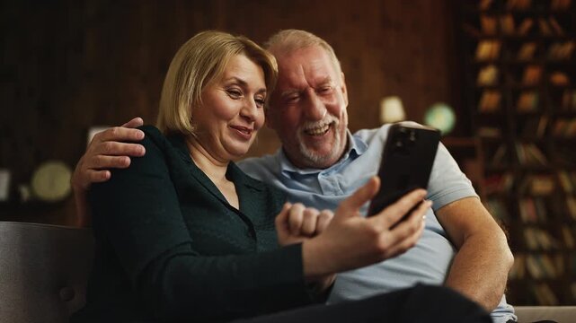 Joyful woman and senior husband watching funny videos on phone social media