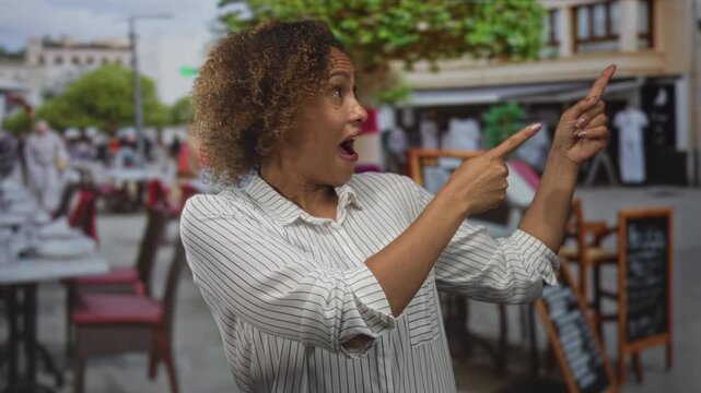 Woman pointing both index fingers at cafe menu boards on a street terrace while smiling with open mouth; joy discovery.