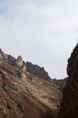 Dramatic rocky peak of Piatra Secuiului mountain with a lone bare tree on the steep slope against a cloudy sky in Rimetea, Romania