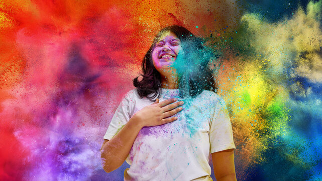 Woman laughing with hand on chest during Holi color explosion. Concept of emotional celebration moment, vibrant festival atmosphere, cultural tradition and lifestyle campaign imagery.