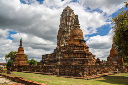 Panorama of Wat Ratchaburana complex in Ayutthaya, Thailand. A weathered prang (tower), flanked by two distinct red-brick chedis (stupas) on a well-maintained green lawn. It's a World Heritage site.
