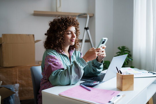 Woman using smartphone at home workspace with laptop and documents