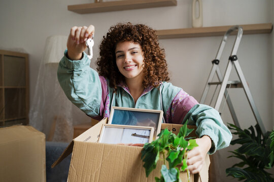 Smiling woman holding keys in new home while unpacking moving box
