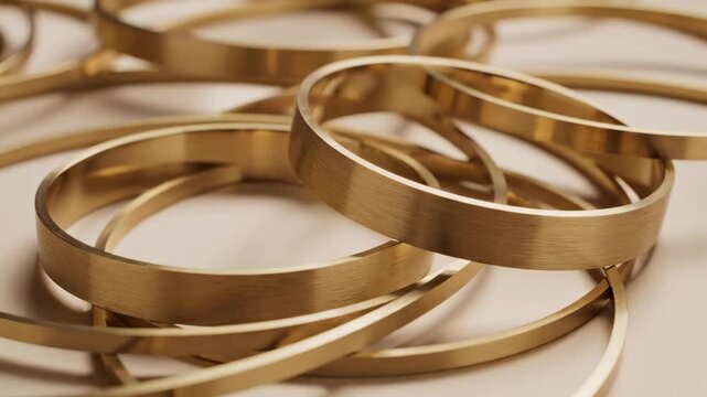 Close-up of brushed brass bangles stacked and intertwined in a soft, neutral background