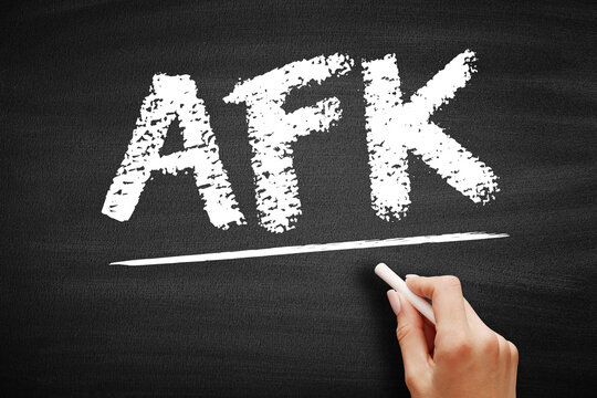 AFK text on blackboard. Gaming slang abbreviation for away from keyboard used in online community chats. Hand holding a piece of chalk on a slate surface