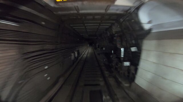 Underground train riding in darkness tunnel. Urban metro driving belowground. Subway train moving at dark tunnel. Point of view from the railway cabin. Transportation of people concept. Slow motion