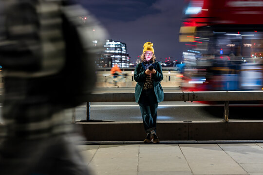 Woman using smartphone at night on London street with city lights