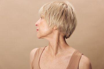 Profile portrait of a mature woman with short blonde hair looking sideways on beige background. Concept of aging, natural beauty, skin texture, and minimalist fashion. © SHOTPRIME STUDIO
