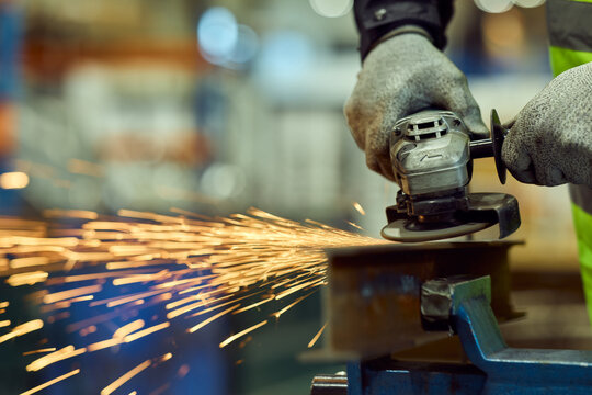Worker Grinding Metal With Angle Grinder Producing Sparks in Industrial Workshop With Safety Gloves