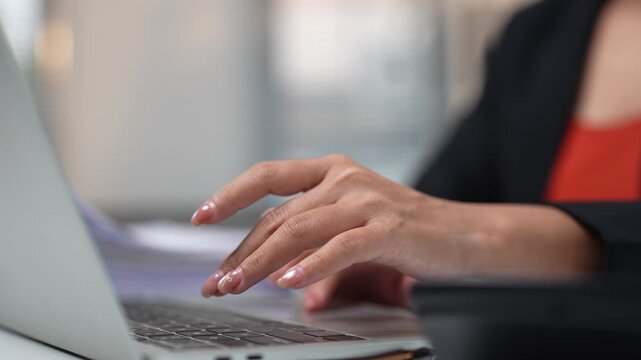 Unrecognizable businesswoman with a professional manicure typing on her laptop keyboard, working on a project in a modern office, focusing on business communication and online research