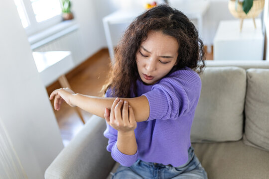 Elbow pain and injury. People with body-muscles problem, Healthcare And Medicine concept. Asian woman sitting on the sofa and holding painful elbow with hand. Joint inflammation and ache concept.