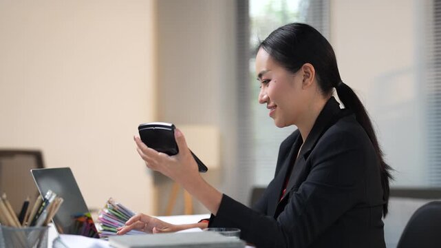Millennial asian business woman sitting at her modern office desk, smiling while using a foldable smartphone for work, communicating and browsing social media during a break from her tasks