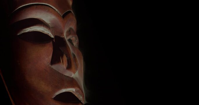 Close-up of carved African mask with drifting smoke on black background and right copy space. Ideal for documentary, exhibition and heritage themes.