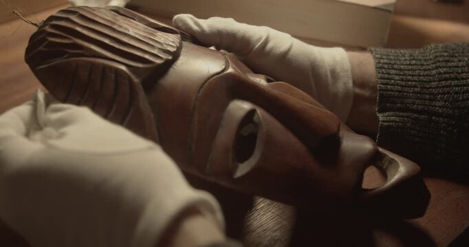 Gloved curator inspecting traditional Baule or Guro mask in museum setting. Ideal for heritage, conservation and exhibition themes.