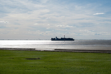 View of the North Sea coast from a green meadow at low tide with a ship