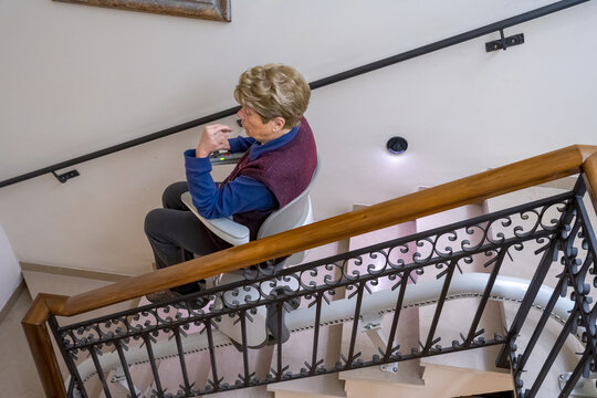Disabled woman seated on home stairlift gliding smoothly down staircase with safety belt engaged