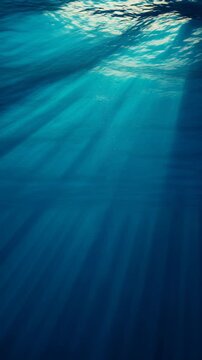 Sunlight rays piercing through deep blue underwater ocean surface with rising bubbles (Vertical Video)