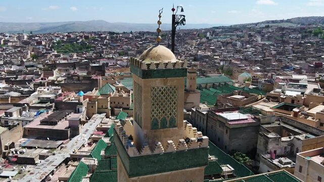Detailed drone close-up of the historic Al-Qarawiyyin mosque minaret. Features the intricate green Zellige mosaic, copper jamour, and a panoramic backdrop of the world's oldest university.