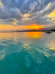 Fototapeta premium Sunset at Issyk Kul Lake in Kyrgyzstan. Bright sun breaking through clouds reflecting in clear turquoise water.