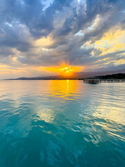 Fototapeta premium Turquoise water of Issyk Kul at sunset with golden reflection and dramatic clouds.