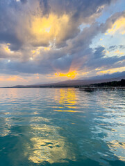 Fototapeta premium Turquoise water of Issyk Kul at sunset with golden reflection and dramatic clouds.