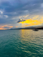 Fototapeta premium Sunset at Issyk Kul Lake in Kyrgyzstan. Bright sun breaking through clouds reflecting in clear turquoise water.