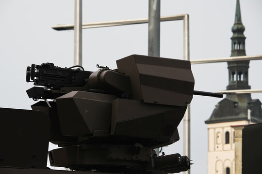 Modern remote controlled weapon station with heavy machine gun mounted on armored vehicle turret against urban city background and cathedral