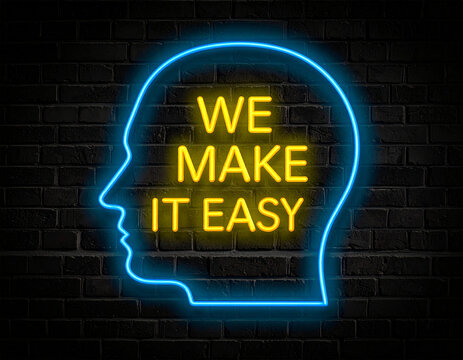 Leuchtende gelbe Neonschrift "We make it easy " umramt von einem blauen Neongesicht auf dunkler Backsteinmauer