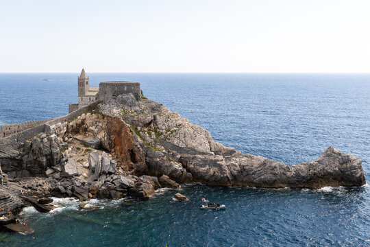 A historic stone church perched dramatically on a rugged cliff overlooking the deep blue sea, surrounded by rocky formations and gentle waves below.