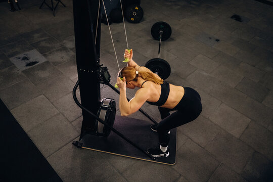 Female athlete performing cable tricep pushdown exercise in a gym, wearing black workout attire and using resistance cables for strength training