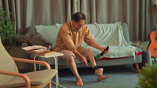 Asian man puts on a prosthetic leg at living room. Amputation and use of an artificial leg.