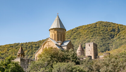 The Church of the Dormition of the Blessed Virgin Mary in Ananuri Fortress stands on a hill surrounded by green trees in Georgia on a sunny day. © denklim