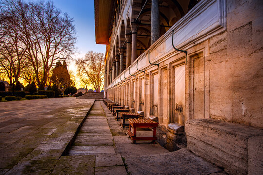 Historic ablution area of a mosque in Istanbul during a warm sunset, with long stone corridors, wooden stools and elegant arches. Peaceful cultural and architectural atmosphere.