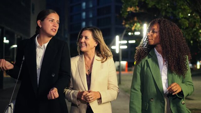 A dynamic trio of women sharing engaging conversation while strolling through the city streets at night, showcasing their camaraderie and connection in a professional setting.