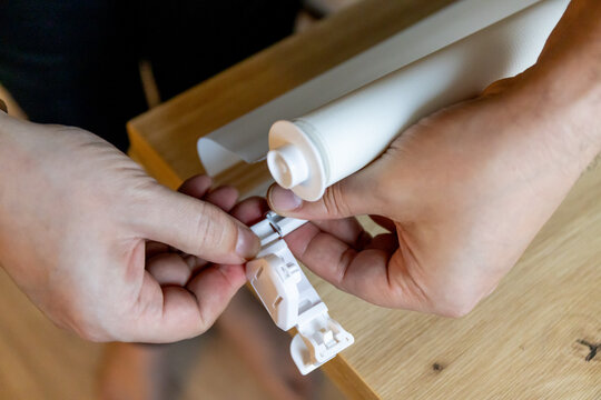 Hands installing roller blinds on windows in details. 