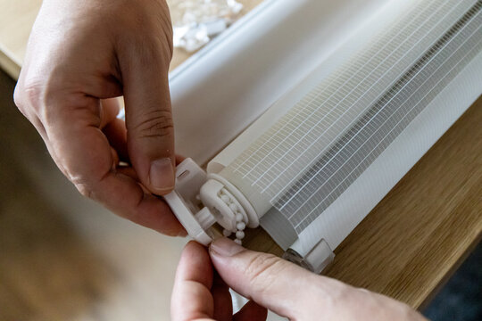 Hands installing roller blinds on windows in details. 