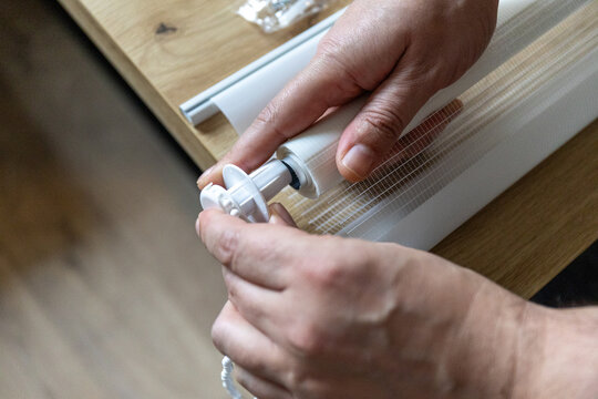 Hands installing roller blinds on windows in details. 