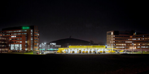 Fototapeta premium Dutch business district at night with delivery van depot dome-shaped arena and illuminated office buildings viewed from across dark field