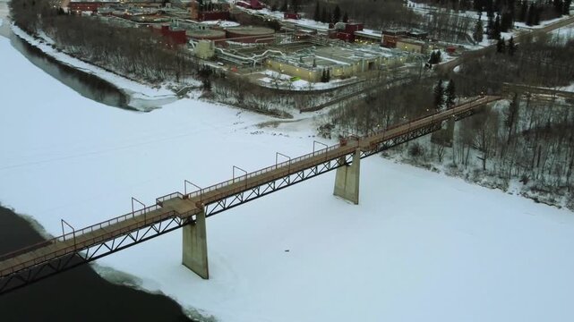 Aerial drone view 18 January 2026 of Bleriot Ferry Bridge spanning frozen Red Deer River in Alberta, Canada, highlighting snow covered winter landscape and remote infrastructure in daylight.