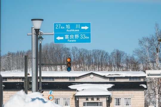 View of crisp winter air and snow-covered rooftops under a blue sky, accented by a blue and white road sign, Biei, Hokkaido, Japan.