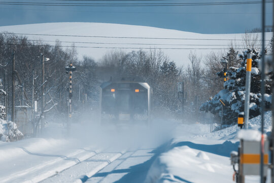 View of a train emerges from a whiteout blizzard, its blurred form a beacon amidst the snowy expanse, a winter journey in progress, Biei, Hokkaido, Japan.