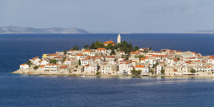 View of a captivating island town with terracotta rooftops and a prominent church tower nestled amidst the deep blue Adriatic Sea, Primosten, Sibenik-Knin County, Croatia.