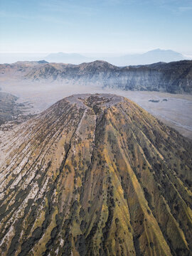 Aerial view of Mount Bromo's majestic volcanic cone rises from the Sea of Sand, a stark contrast against the distant blue sky, East Java, Indonesia.