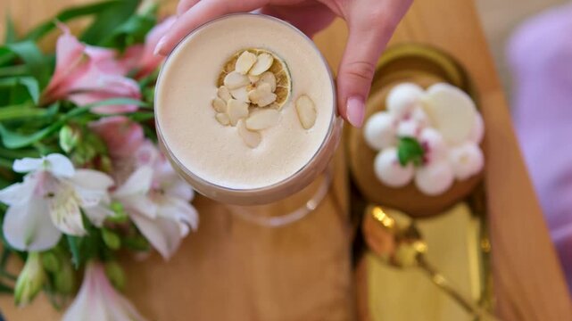 a woman's hand taking a glass breakfast, dessert with airy white cream, coffee drink, orchid flowers in glass on wooden table, a wonderful dessert in a luxury restaurant, relaxation, pleasure, wealth.