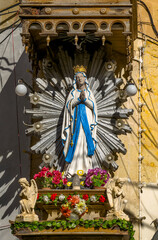 Naklejka premium Outdoor statue of Virgin Mary with blue robe and radiant halo on historic building facade