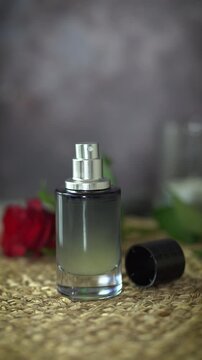 Close-up vertical video of black perfume bottle without cap and red rose on dark and beige background. Luxury fragrance presentation with natural homemade essential oil perfume concept.