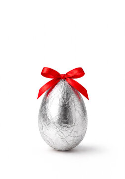 Silver foil wrapped Easter chocolate egg with red ribbon bow isolated on white background. Minimal festive composition, luxury holiday concept with copy space and clean high key studio lighting.