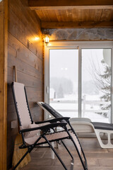 Vertical shot of a cozy mountain lodge interior with folding deckchair and snowy terrace view.