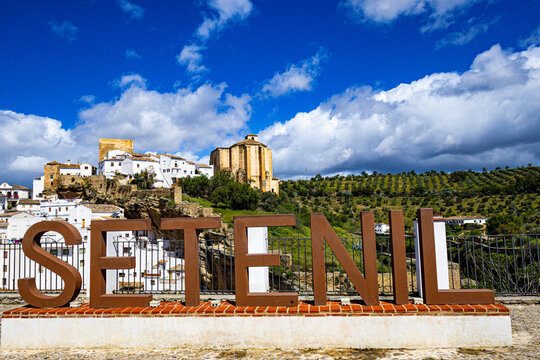 View of whitewashed houses nestled beneath a rocky overhang, contrasting with the bright blue sky in Setenil de las Bodegas, Andalusia, Spain.