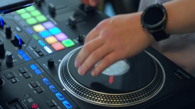 Real-time close-up of DJ hand scratching spinning jog wheel on turntable controller, colorful illuminated performance pads, blue LED buttons, faders, knobs visible during live set
